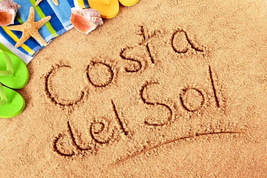 Costa del Sol written on the sand with shells and a towel