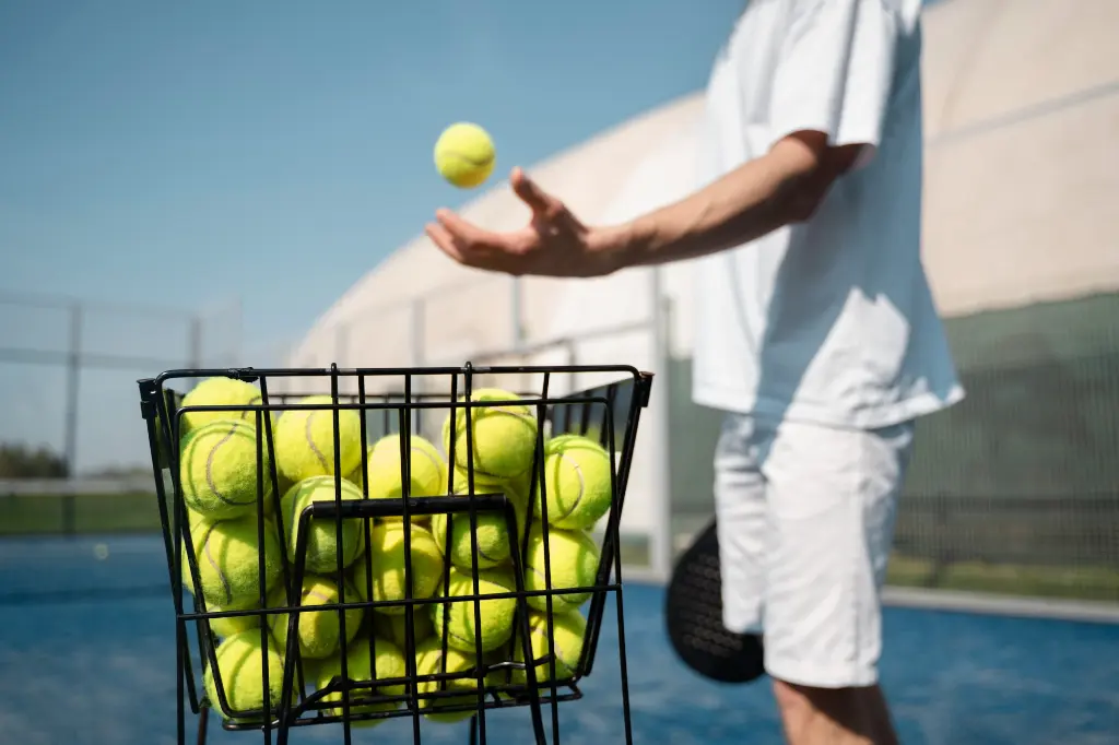 Side view of a padel tennis coach with white shirt taking a yellow ball from a basket