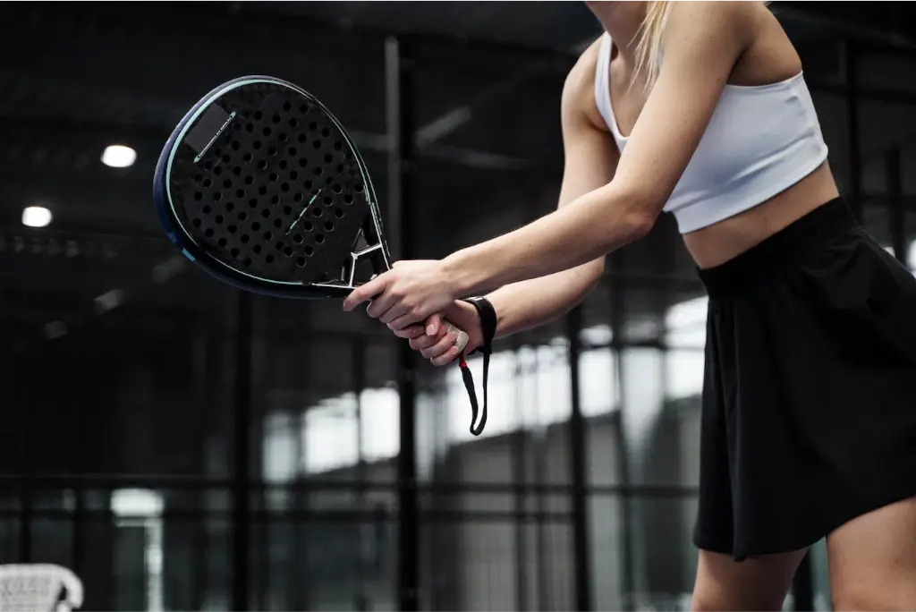 Side view of a woman playing padel tennis with a black racket white top shirt and black skirt