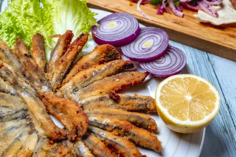 Traditional pescaitos fritos fried anchovies from Malaga with lemon onions lettuce on a wooden table